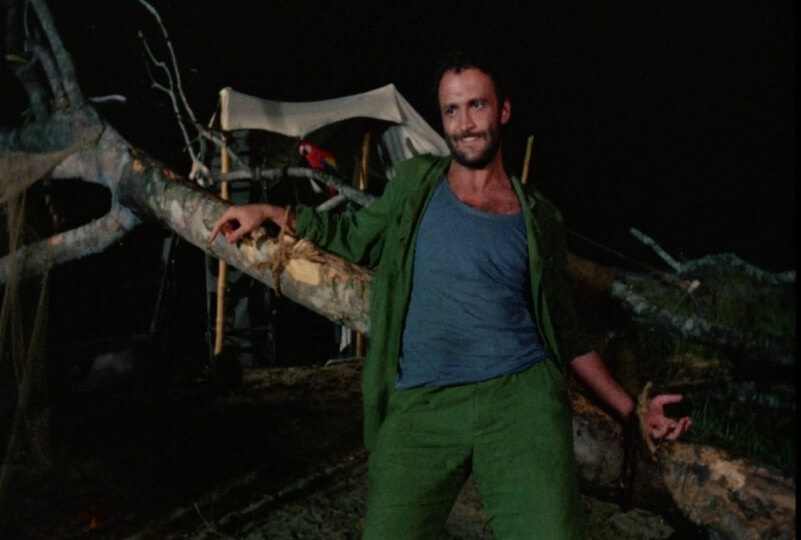 A man sneers while bound to a tree in Eaten Alive, one of our 11 Best Cannibal Movies.