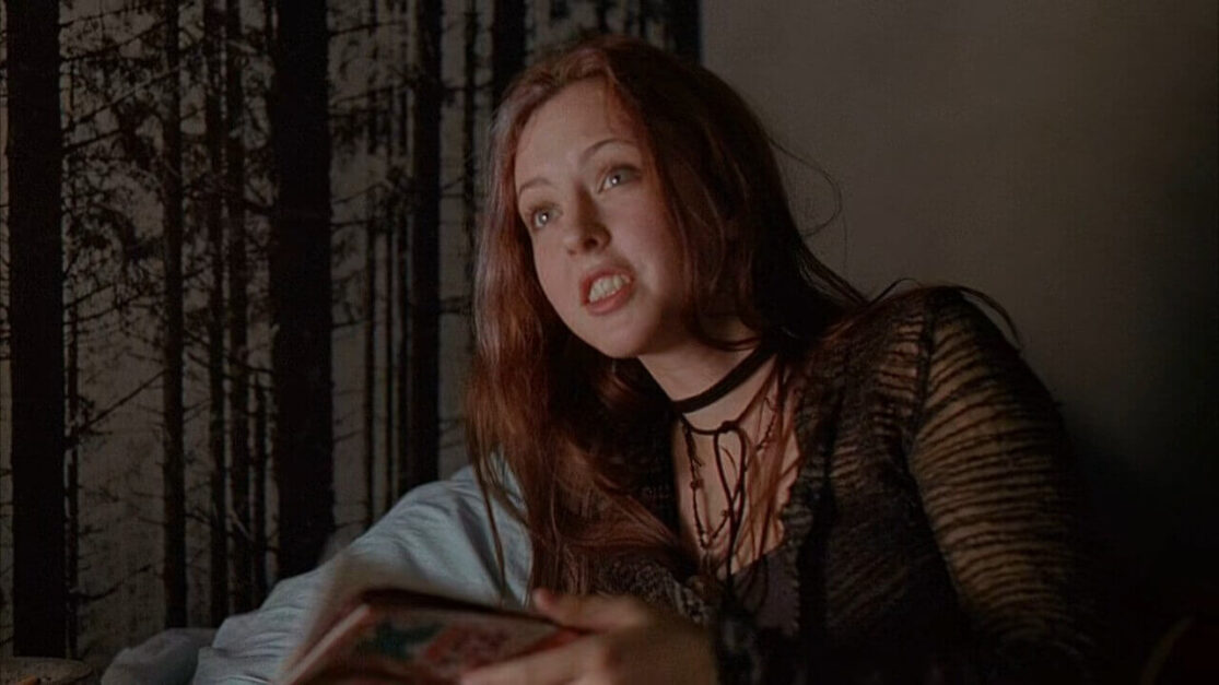 An agitated young woman on a bed thumbs through a book.