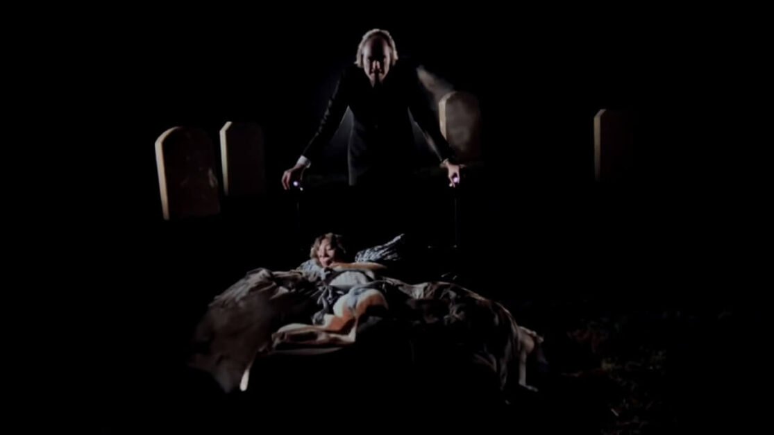 In a dream sequence, a tall sinister-looking man flanked by headstones looms over the bed of a terrified boy.