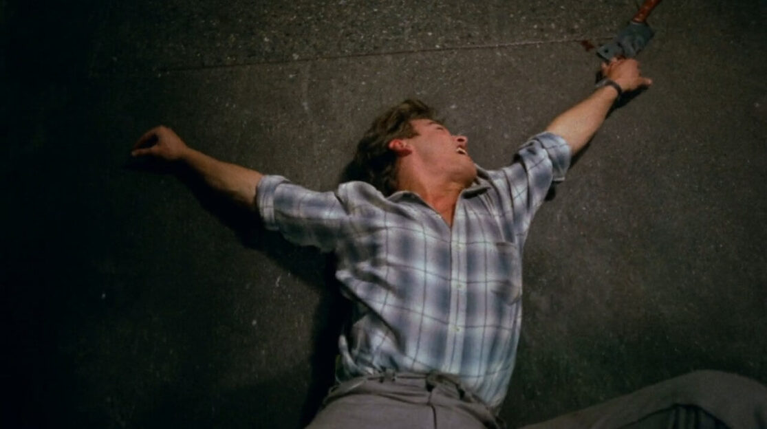 A man in a flannel shirt frantically reaches for a meat cleaver as an unseen person drags him across the floor.