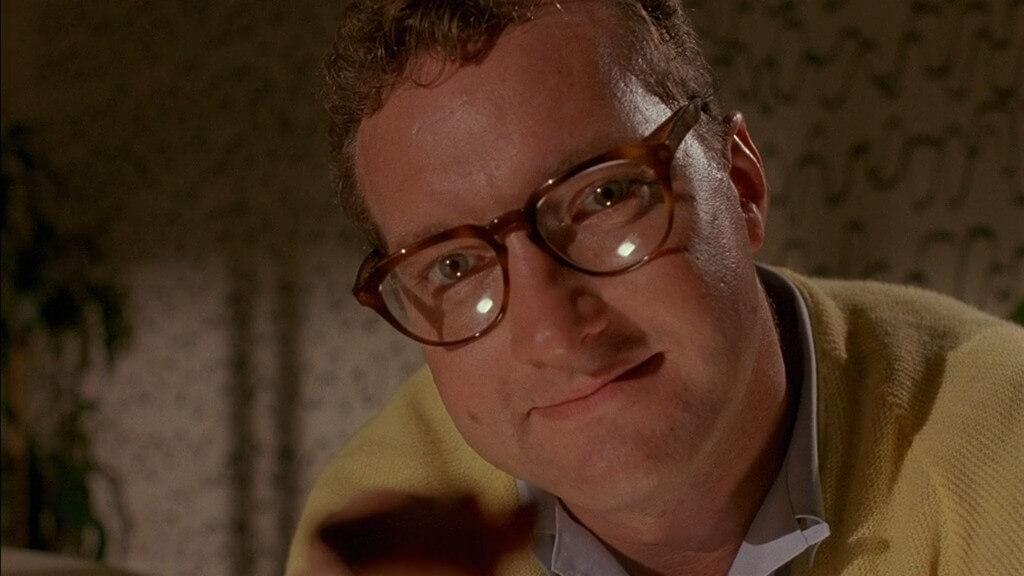 A man in glass smiles while offering a bite of whatever's on his fork.