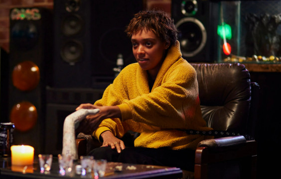 A young woman in a yellow sweater sits in a chair. She holds a ceramic hand on the coffee table before her.