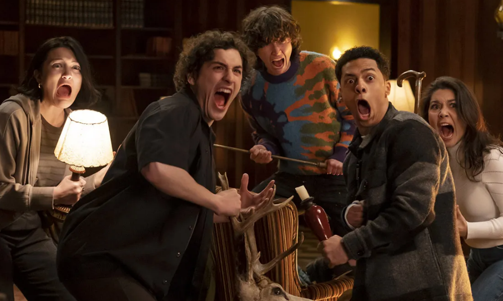 Five teenagers scream in fear at something just offscreen.