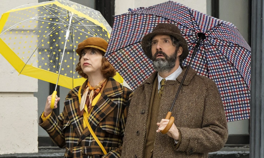 Kristen Schaal and Tony Hale holding umbrellas and looking upset.