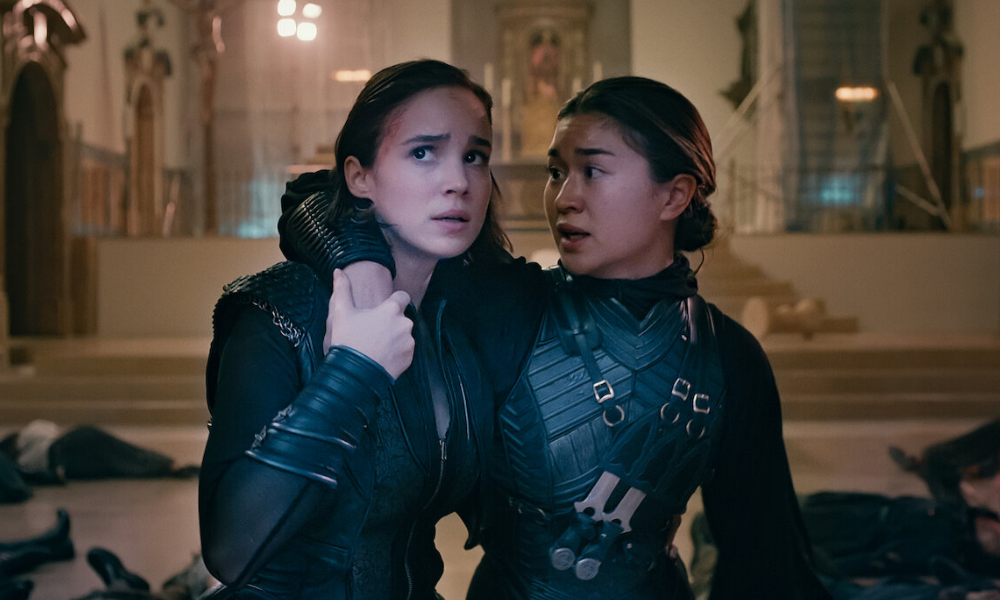 One warrior nun wraps an arm around another; they both look worried.