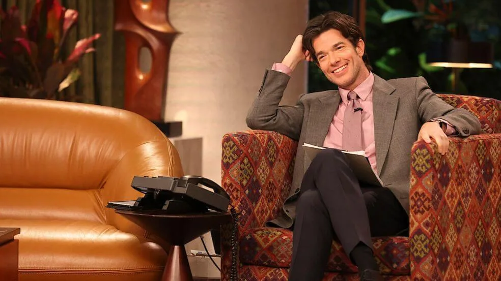 Image of host John Mulaney sitting in a chair on the set of Everybody's Live with John Mulaney.