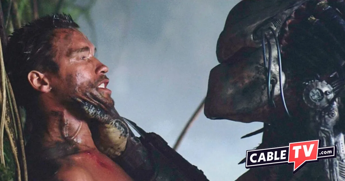 A predator has Arnold Schwarzenegger backed up against a tree in a scene from Predator (1987).