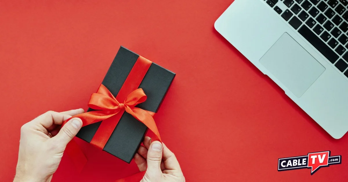 Overhead view of hands holding a small gift box with a red bow and part of laptop keyboard