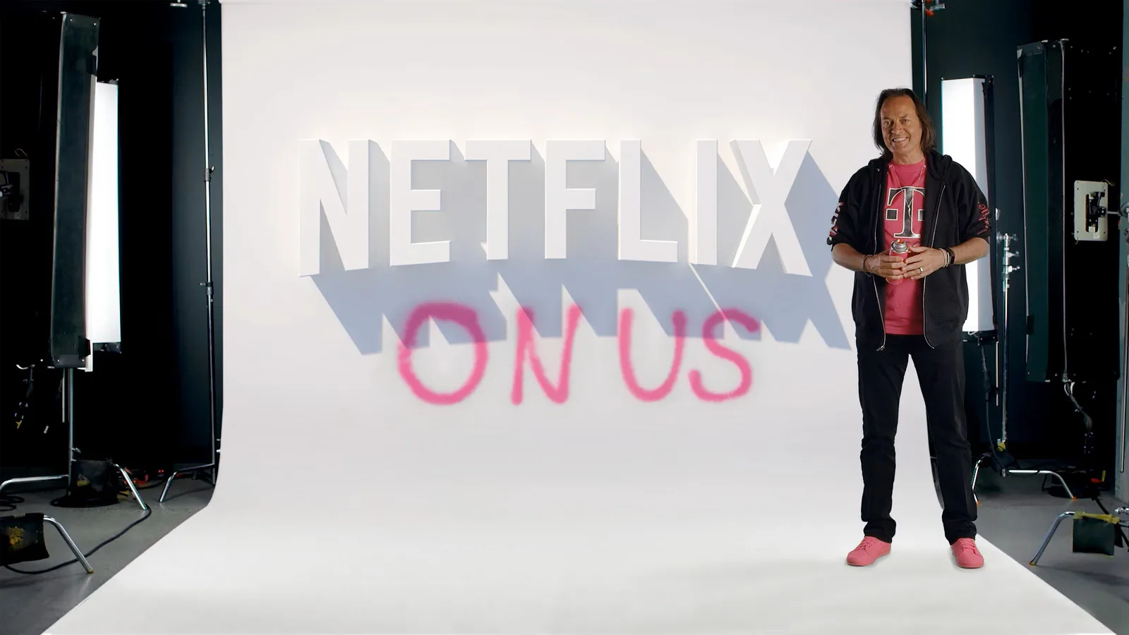 A man standing in front of the Netflix logo with “ON US” written below in spray paint.