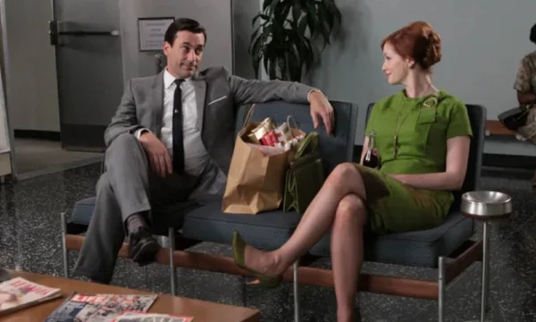 A man and a woman smile at each other from waiting room chairs.