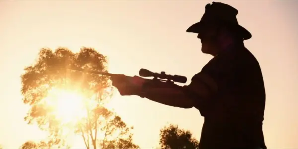 Image of a man outdoors at sunset holding a rifle in Wolf Creek.